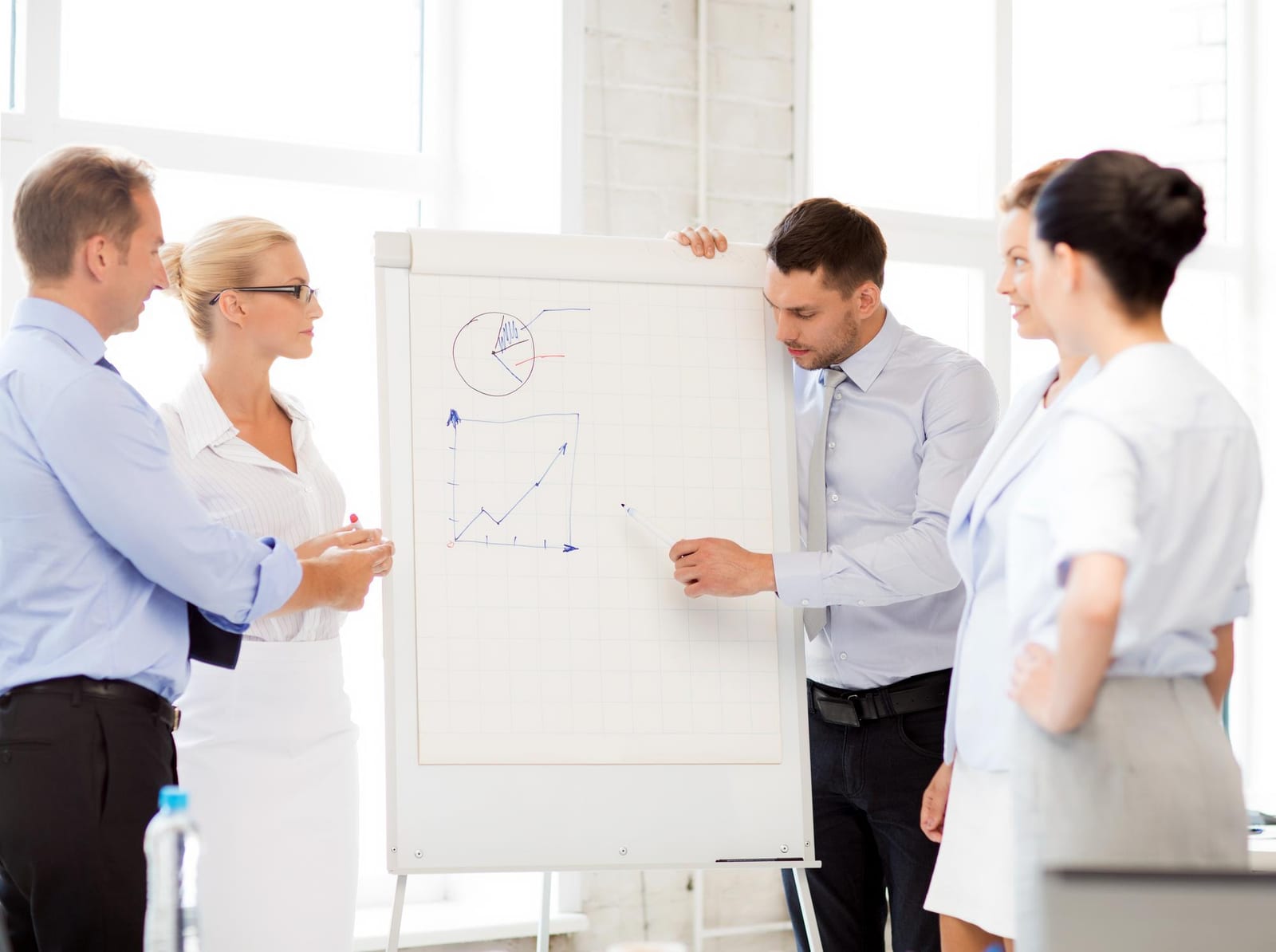 Quatro profissionais analisam gráficos desenhados em um flipchart em pé.